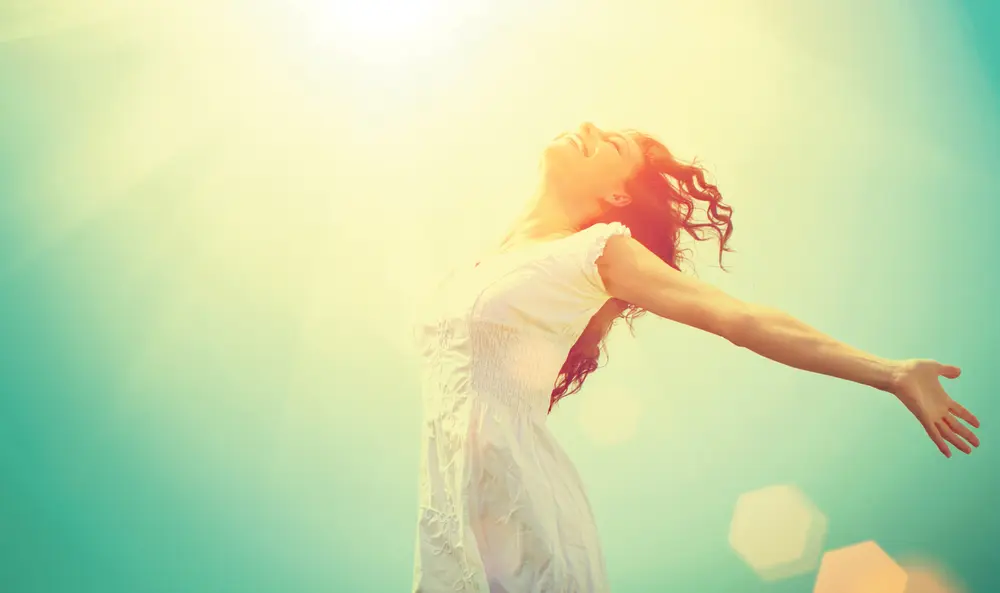 Woman with outstretched arms enjoying sunlight and nature.
