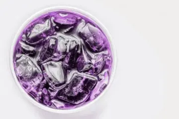 Purple liquid with ice cubes in a clear glass on a white background.