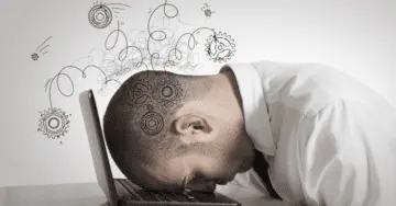 Man with head on laptop overwhelmed by technology stress.