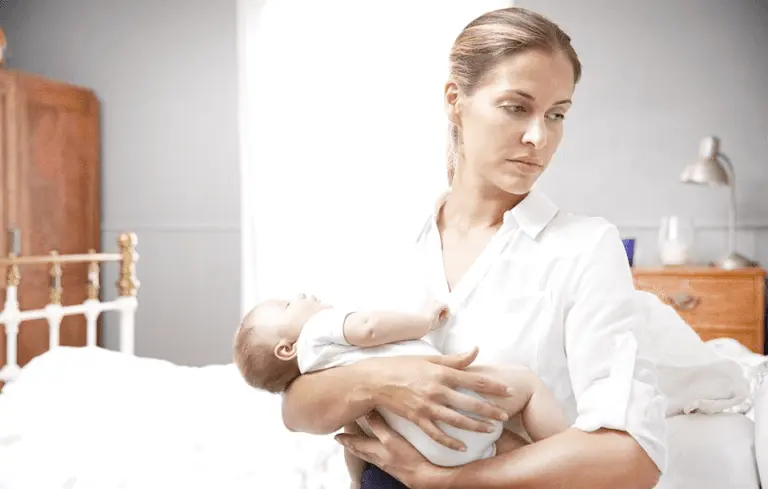 Mother holding a baby in a bright, calm bedroom setting.