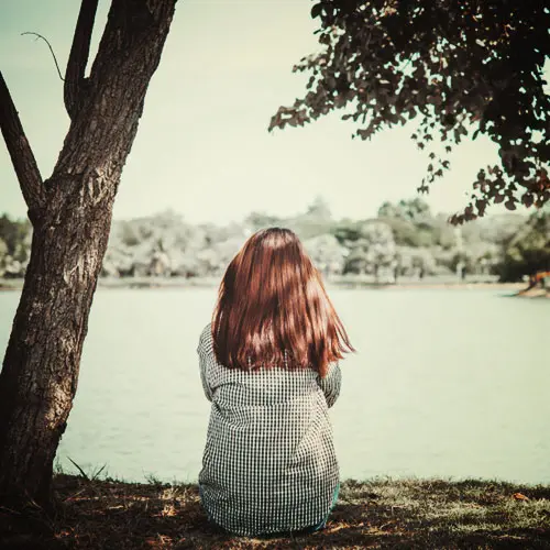 Woman sitting by a lake, enjoying nature and mental wellness.