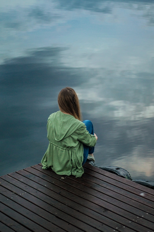 woman sitting on dock by a lake