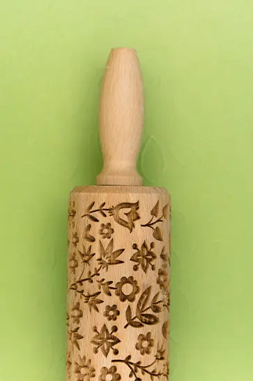 Decorative wooden rolling pin with floral carvings for baking or crafting.