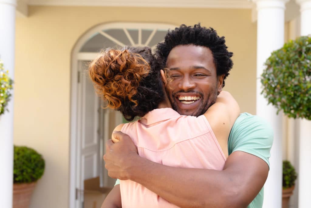 Cheerful young african american man hugging girlfriend against house. people, love and togetherness