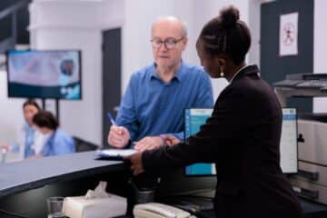 Rception worker standing at hospital counter discussing medical expertise with a patient