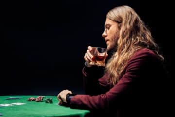 man in eye glasses holding glass with whiskey at a poker table