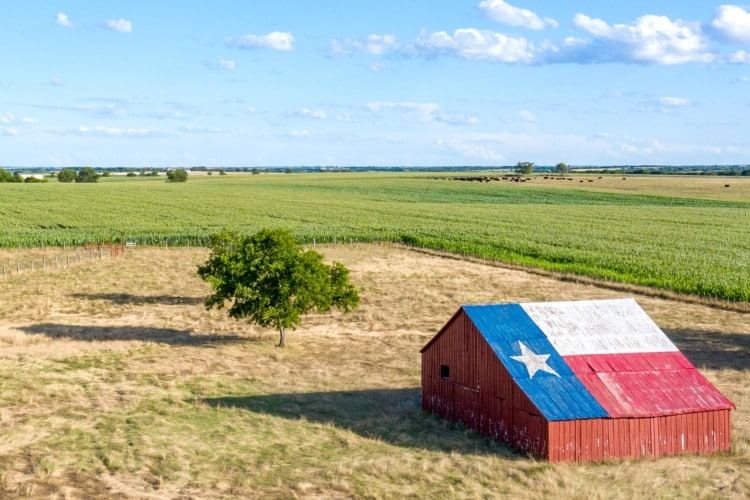 Barn with the symbol of Texas painted on the roof sits in a rural area of the state, framed by farmland.