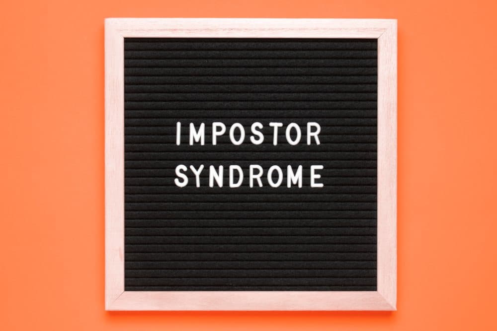 The word Impostor Syndrome on a letter board over an orange background