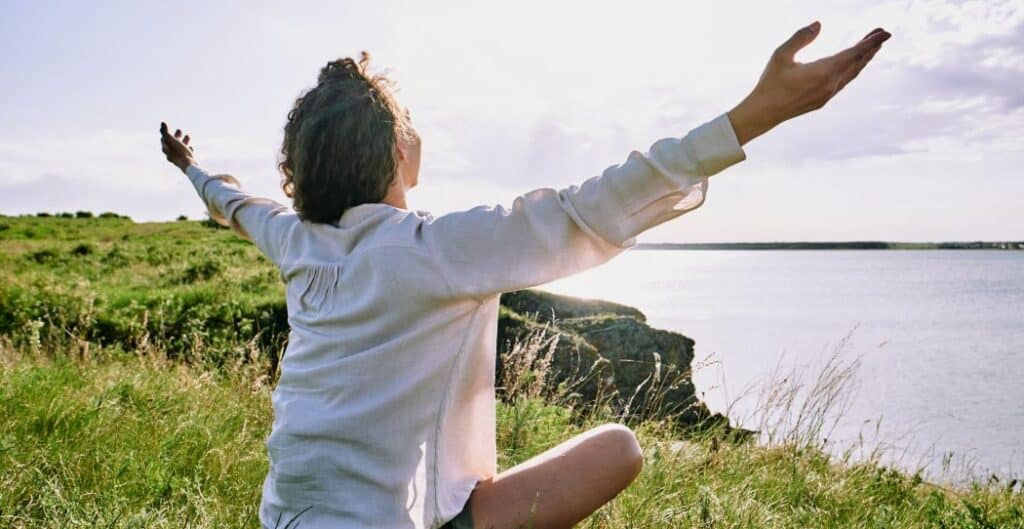 woman with outstretched arms sitting on the ground covered by the ocean