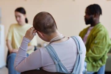 Rear view of shaved woman sitting with group at psychotherapy session in office