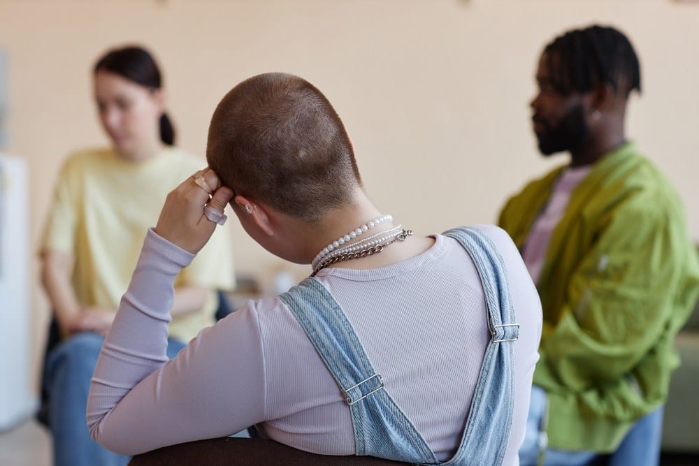 Rear view of shaved woman sitting with group at psychotherapy session in office