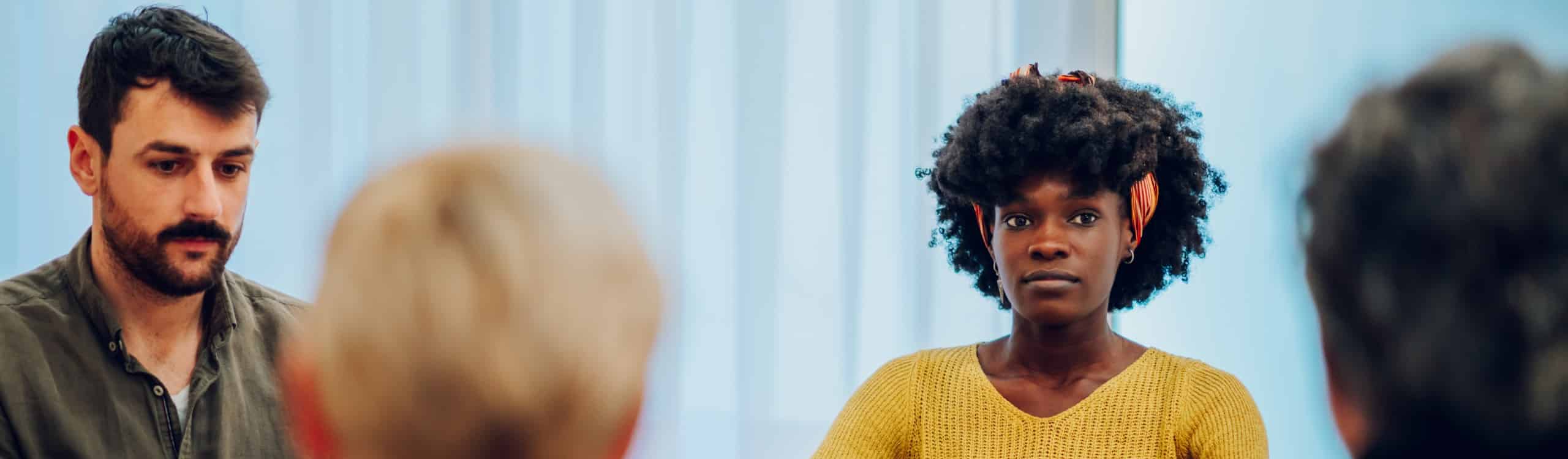 Diverse group of patients gathered in circle at psychologist office discussing self problems while listening others. Getting psychological support. Focus on an african american woman with afro hair.