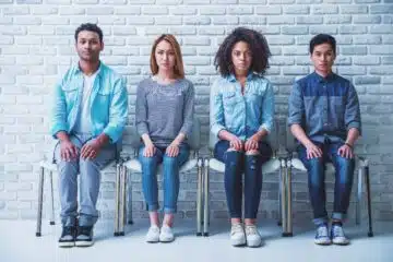 Young people of different nationalities are looking at camera while sitting with hands on knees in