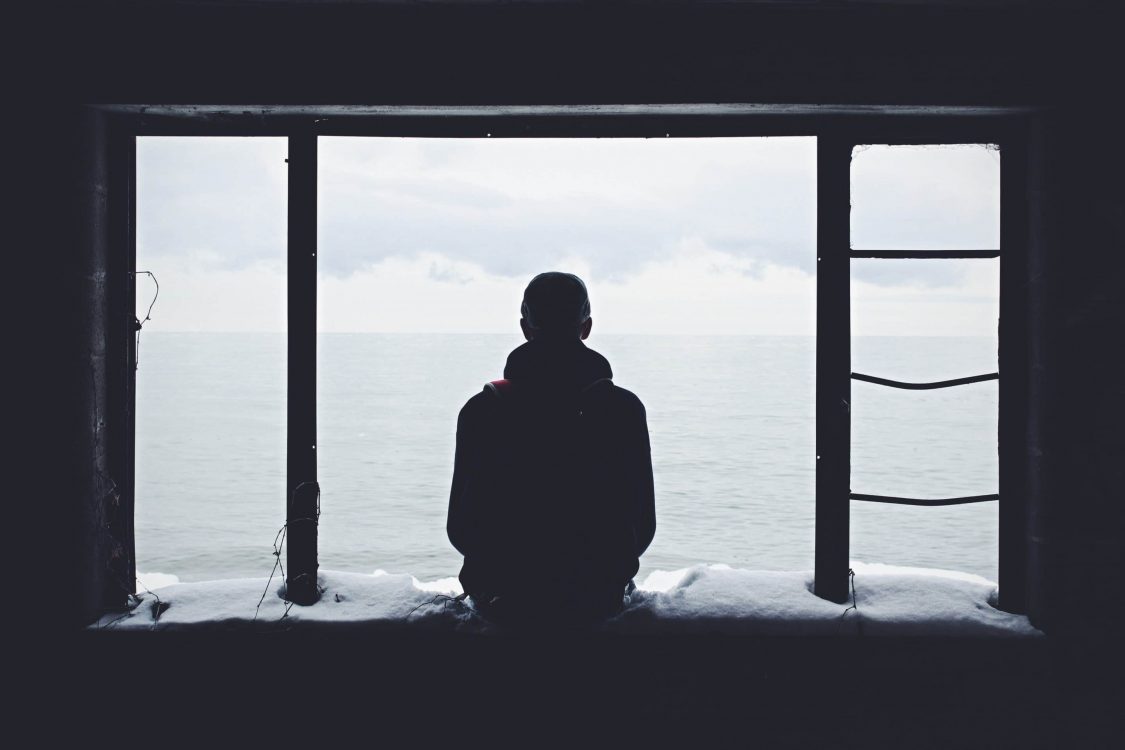 Person sitting alone by the window overlooking the ocean.